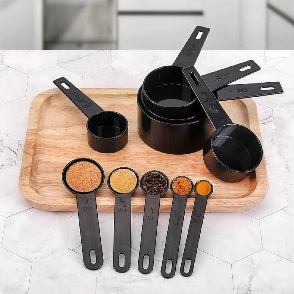 Plastic measuring spoons and cups on a wooden tray, filled with various spices, displayed on a white hexagon-tile kitchen counter.