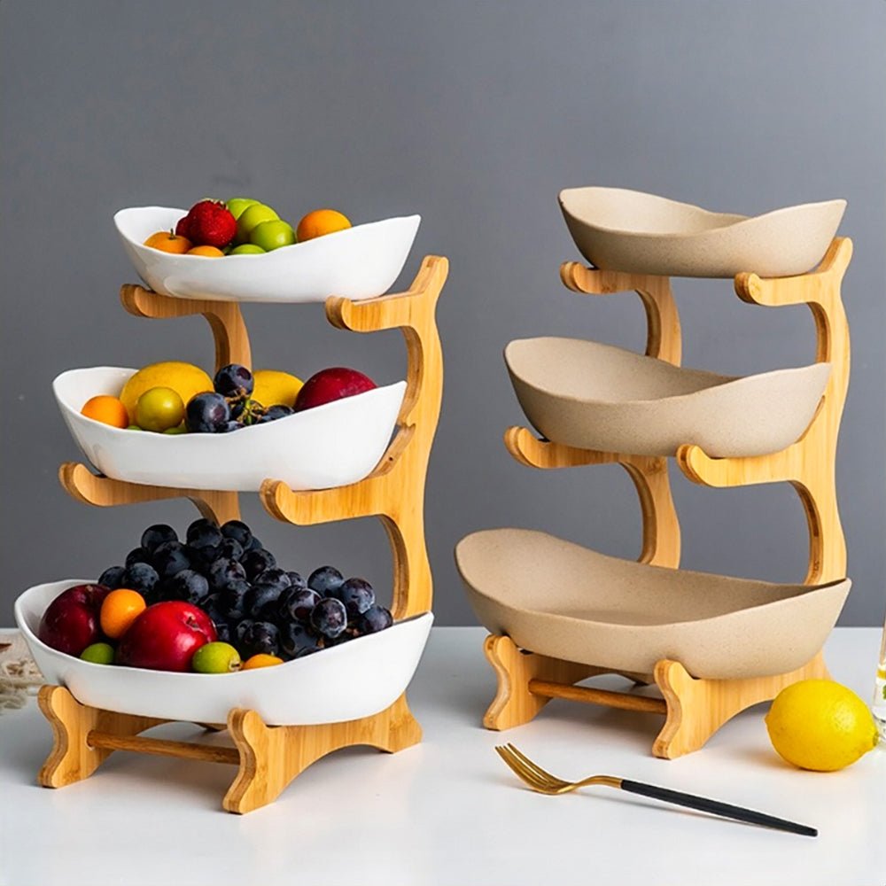 A 3-tiered fruit bowl display on a dining table, featuring a silver-pink fruit bowl and a white fruit bowl, both overflowing with fresh fruits.