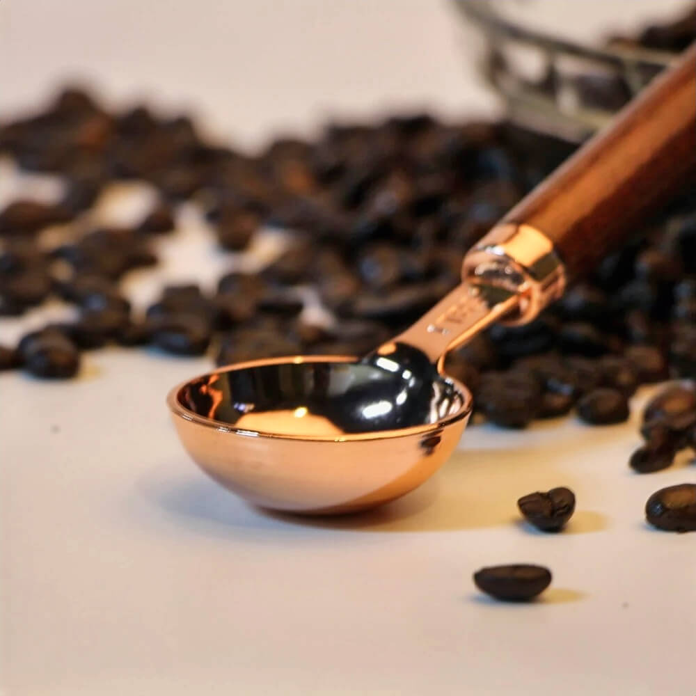 A close-up of a 300 mg rosin measuring spoon with a sleek copper-plated, non-stick surface and a smooth wooden handle. The spoon is surrounded by scattered coffee beans, creating a warm, inviting atmosphere perfect for precise measurements and stylish functionality.