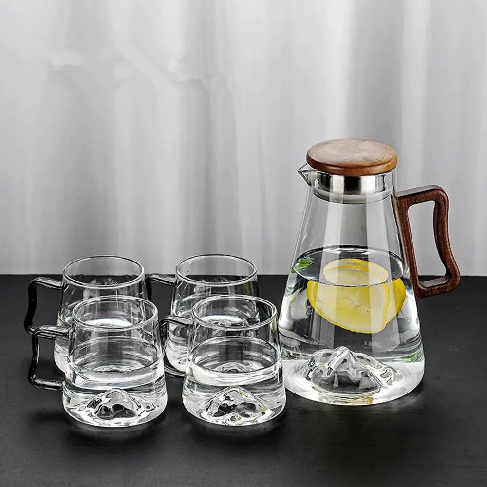 Clear glass tea set with wooden handle and lid on a dark surface.