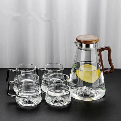 Clear glass tea set with wooden handle and lid on a dark surface.