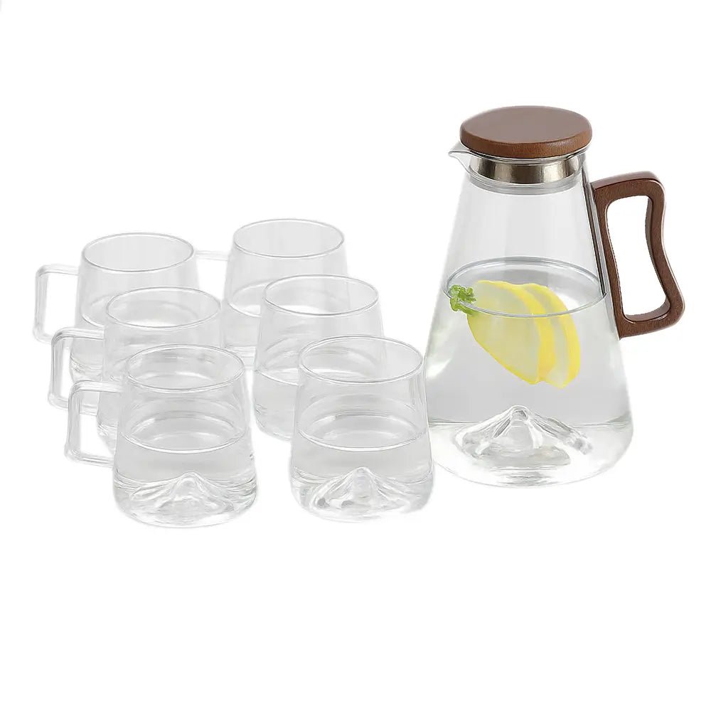 Clear glass carafe with wooden handle and lid, surrounded by six clear glass mugs on a white background.
