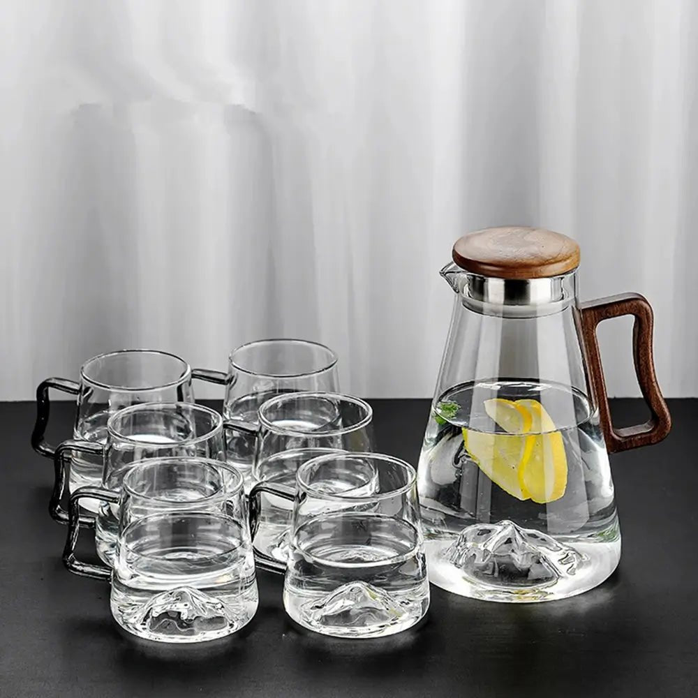 Set of glass mugs and a glass carafe with wooden lid and handle on a dark surface.
