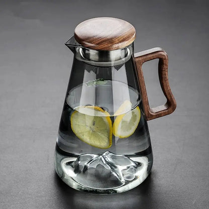 Glass pitcher with wooden lid and handle containing lemon slices and ice on a gray background.