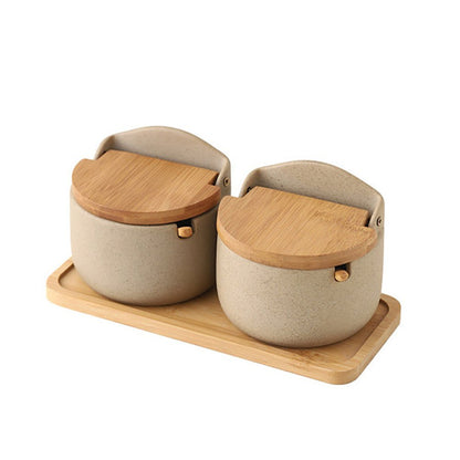 Set of two condiment jars with wooden lids, spoons, and wooden tray.