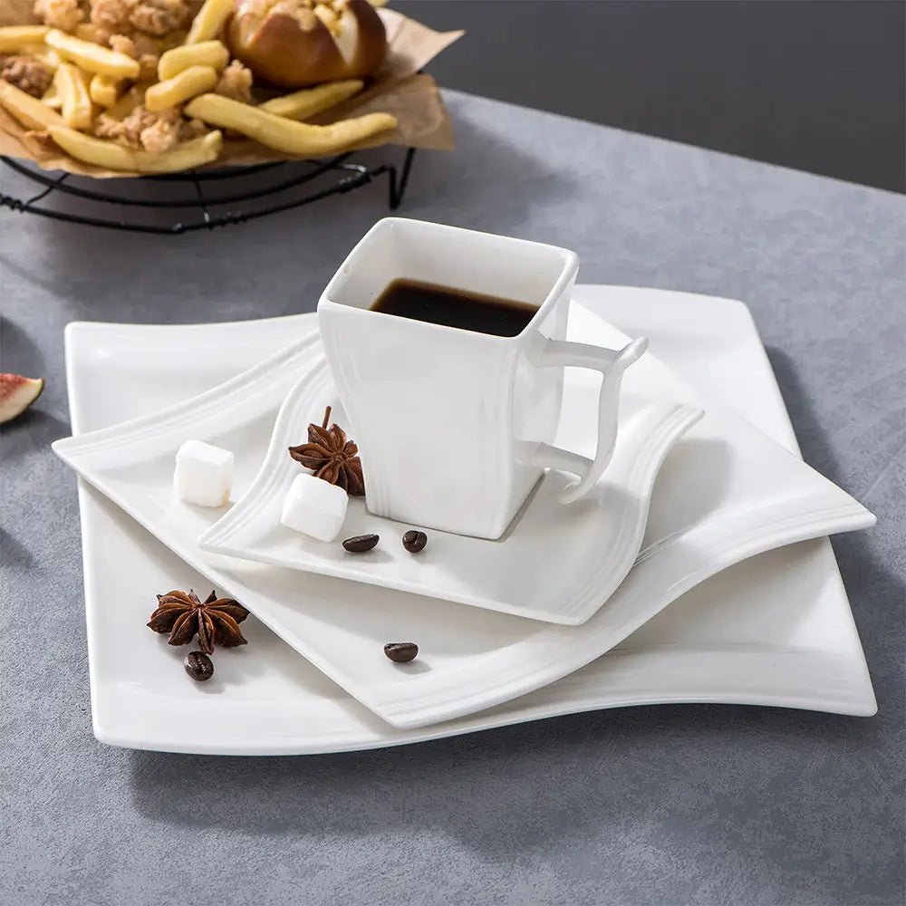 White ceramic cup and saucer with coffee on a gray surface, surrounded by fries and bread.