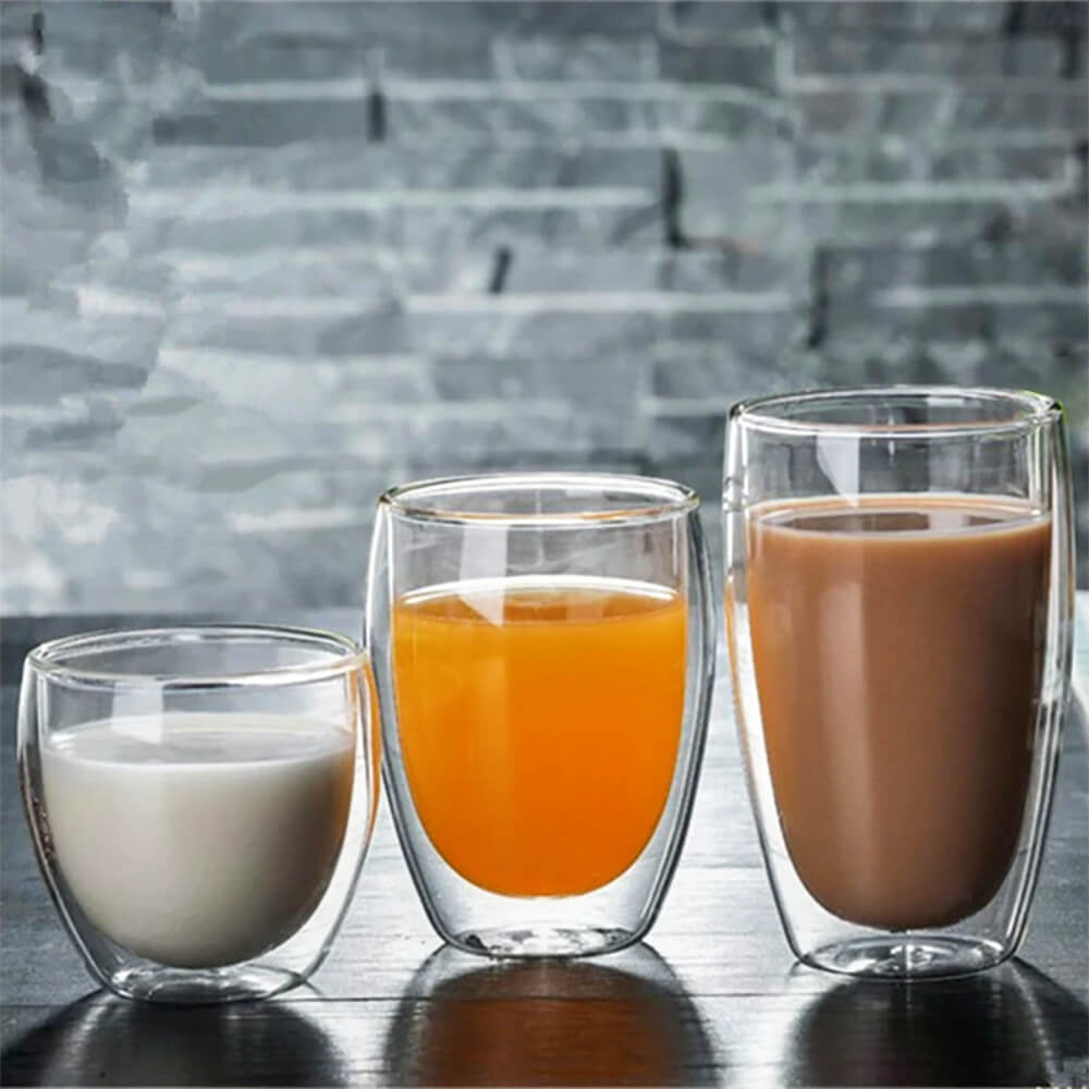 Three of the best double walled espresso cups in different sizes are filled with milk, orange juice, and coffee, set against a gray textured background.