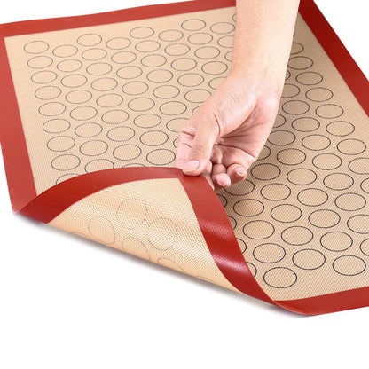 Hand holding flexible best macaron silicone baking mat with circular guides, non-stick surface, and red border for easy lifting.
