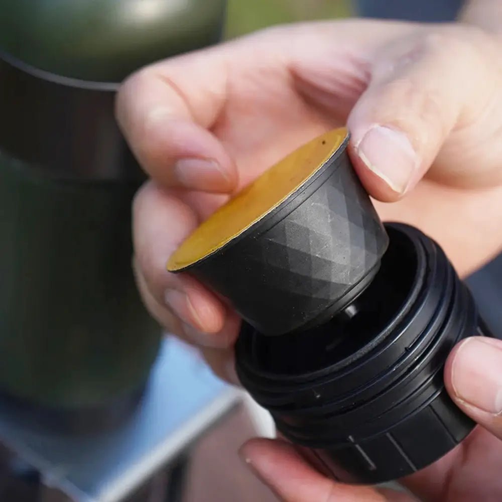 Person holding a black and gold cylindrical espresso capsule.
