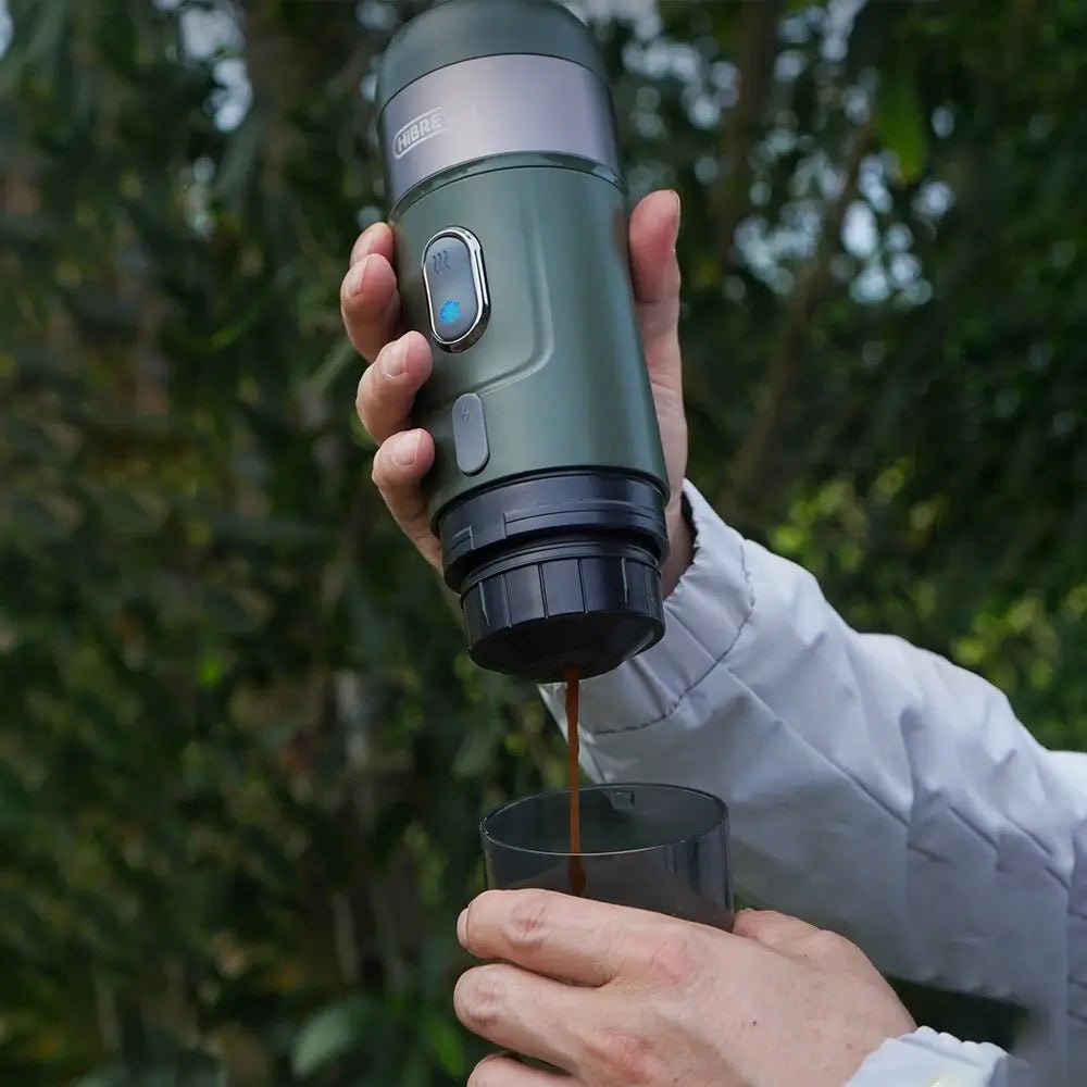 Person pouring coffee from a portable coffee maker into a cup outdoors.