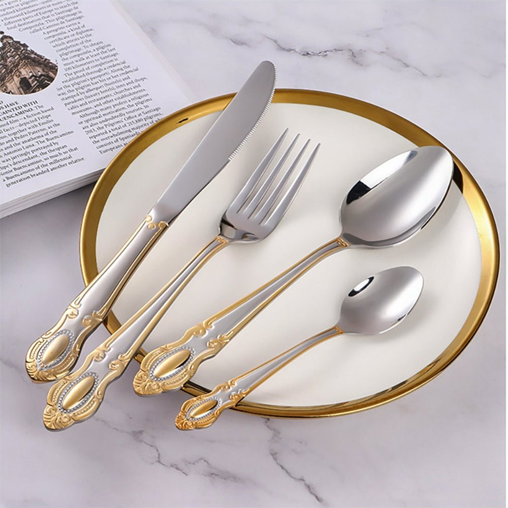 Gold-accented vintage flatware set on a white plate with a gold rim, placed on marble beside an open magazine.