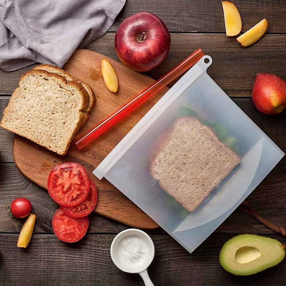 The best reusable silicone bag holding a fresh sandwich, surrounded by a tomato, avocado, apple, and a pinch of salt on a kitchen counter.