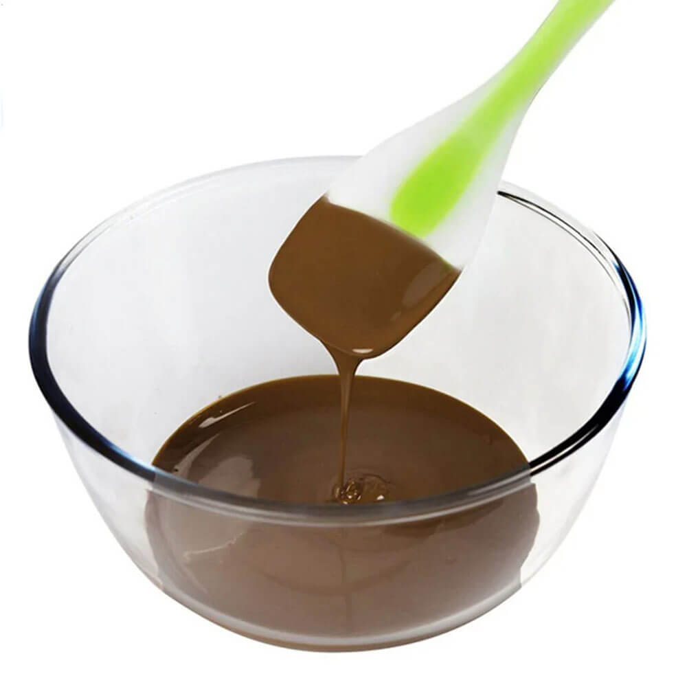 A close-up of a silicone spatula from the best silicone utensils set being used to stir or mix melted chocolate in a clear glass bowl. The spatula features a green and white seamless silicone design, showcasing its flexibility and smooth surface for precise mixing.