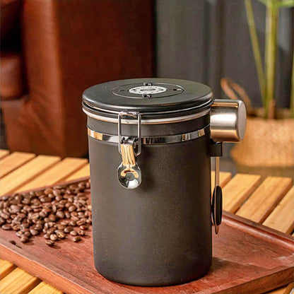 A black, airtight best stainless steel food storage container with a secure latch, built-in date tracker, and attached stainless steel spoon, placed on a wooden tray with coffee beans in a cozy setting.