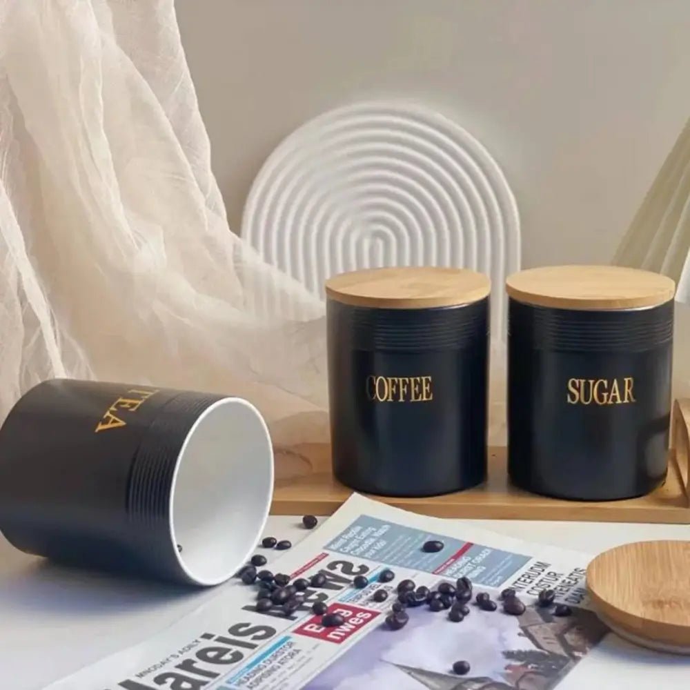 Black tea coffee sugar canisters with bamboo lids on a tray, one tipped over spilling coffee beans onto a newspaper.