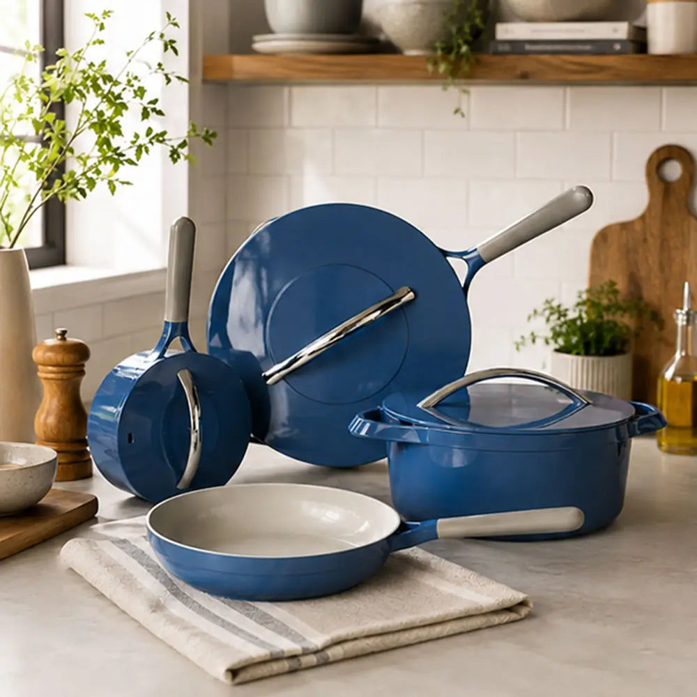 Blue ceramic cookware set including a frying pan, saucepan, stockpot, and glass lid displayed on a kitchen countertop.