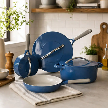 Blue ceramic cookware set including a frying pan, saucepan, stockpot, and glass lid displayed on a kitchen countertop.
