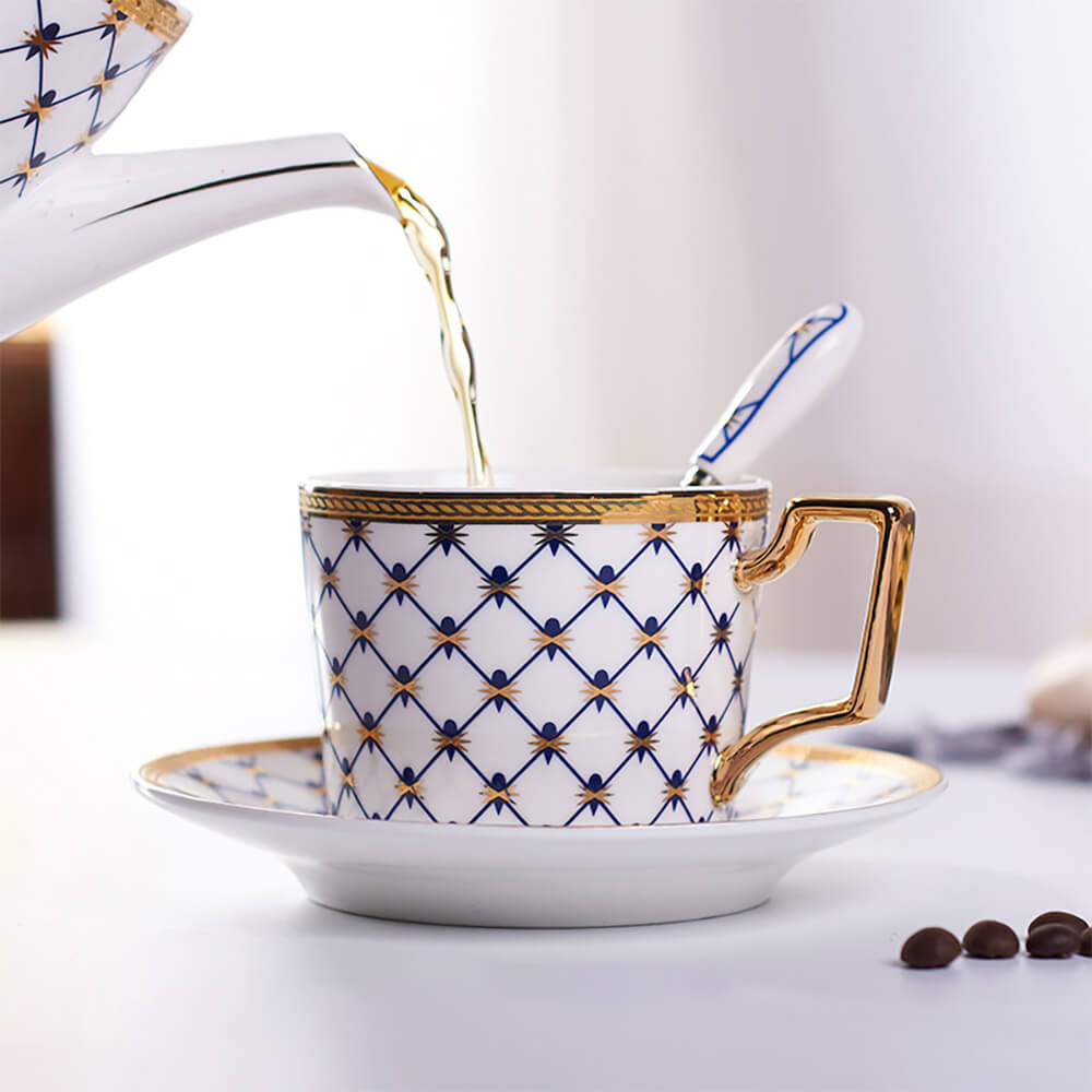 A sophisticated blue tea cup from the honeycomb tea set, adorned with a honeycomb pattern and golden accents. Tea is being elegantly poured into the cup, paired with a matching saucer and spoon for a luxurious tea experience.