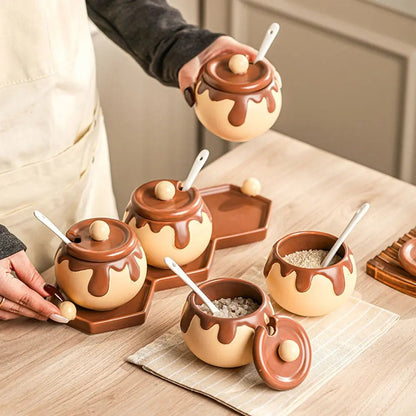 A hand places a brown and beige chocolate-drizzle-style ceramic canister for kitchen storage onto a wooden table with three others.