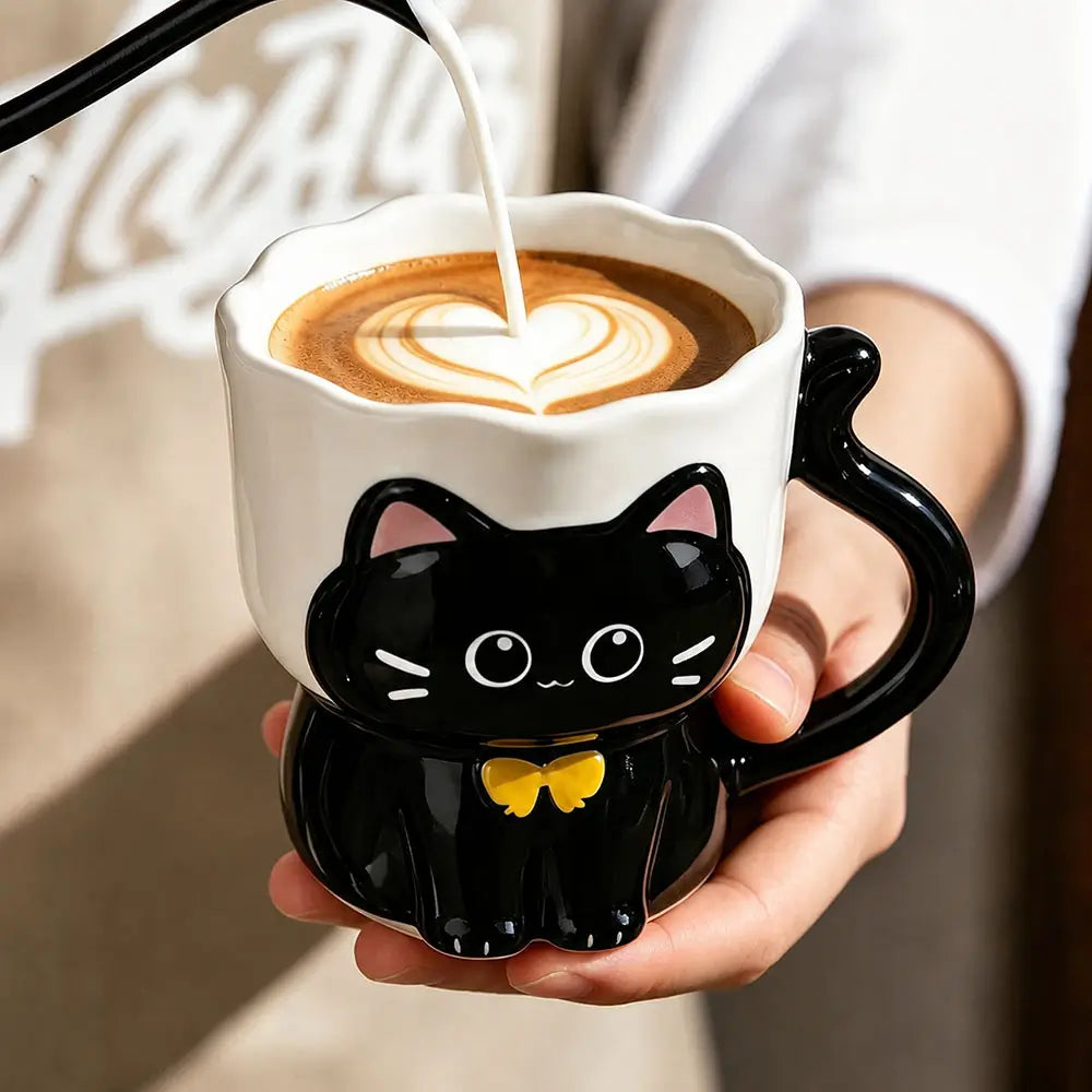 A person holds a white ceramic coffee mug shaped like a black cat with pink inner ears, white facial details, and a yellow bow tie. A pour-over coffee is being poured into the mug, which already contains latte art.