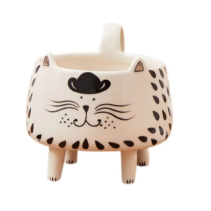  A ceramic mug shaped like a cat with a whimsical design, featuring a black cowboy hat, a smiling face with whiskers, and black teardrop-shaped patterns on its body. The mug stands on four short legs and has a handle at the back.