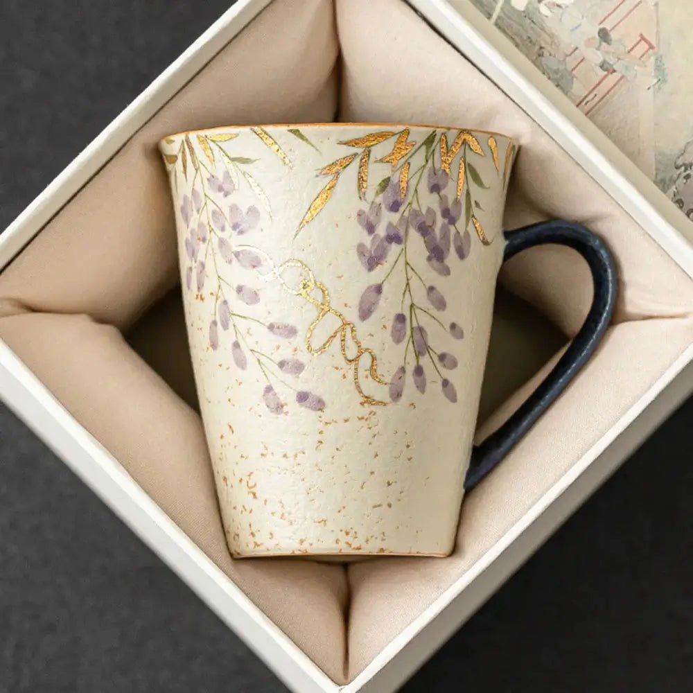 Ceramic mug with floral pattern and dark handle placed inside a padded gift box, viewed from above on a dark background.
