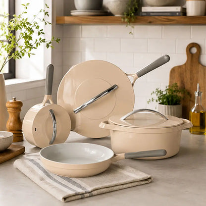 Beige ceramic cookware set featuring a frying pan, saucepan, stockpot with glass lid, and matching lids displayed on a kitchen countertop.
