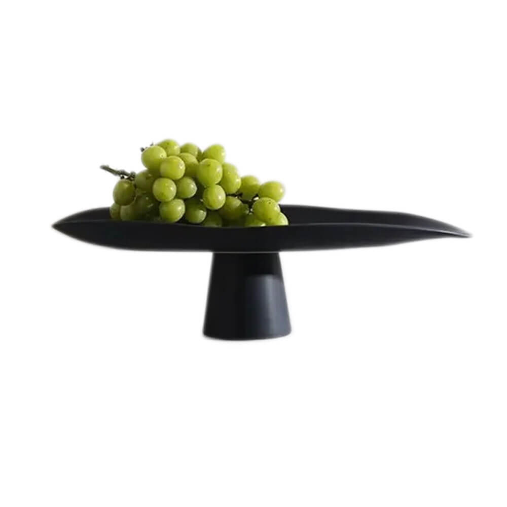 A sleek black ceramic fruit bowl with a minimalist design, featuring a wide, curved surface on a sturdy pedestal base, elegantly displaying green grapes.