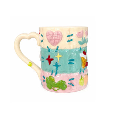 Colorful ceramic latte mug with a heart-shaped handle, pastel glaze and raised decorative motifs on a light background.