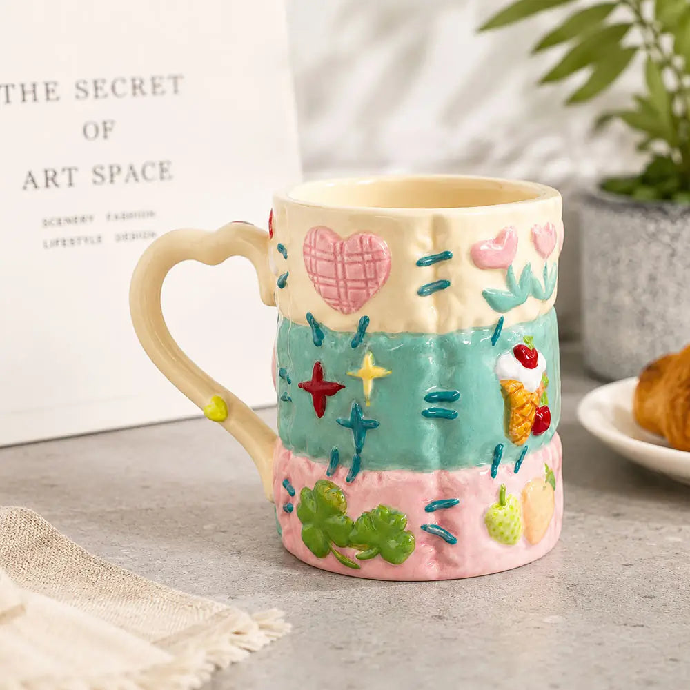 Colorful ceramic latte mug with a heart-shaped handle, raised floral and fruit motifs, and a glossy handcrafted finish.