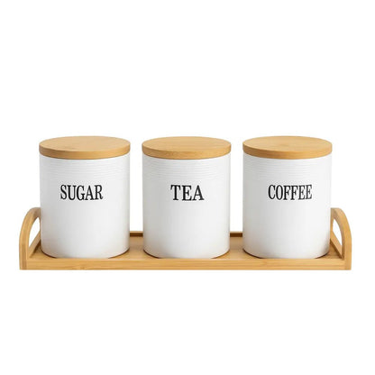 Ceramic tea coffee sugar canisters with bamboo lids arranged on a wooden tray against a white background.