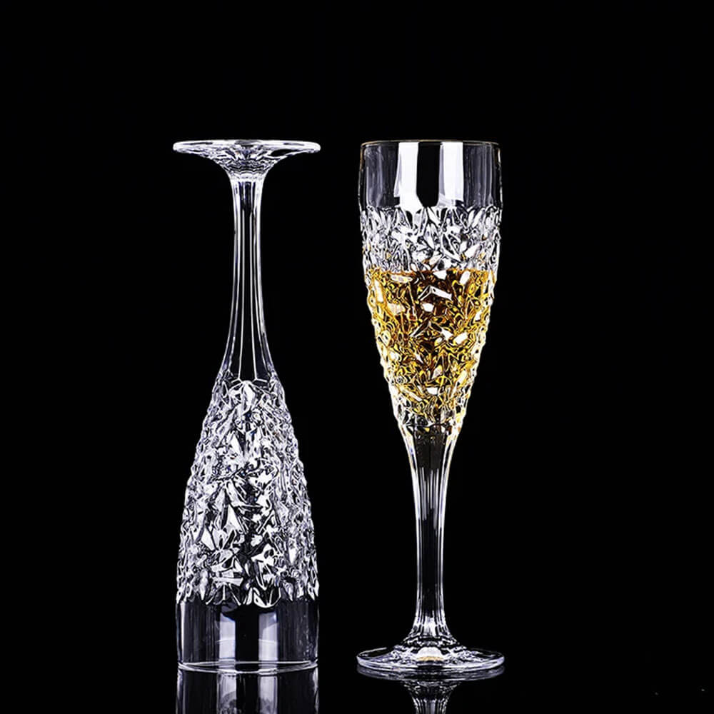 Two elegantly designed plastic flute glasses featuring intricate faceted detailing, one upright filled with a golden liquid and the other positioned upside down, set against a sleek black background.