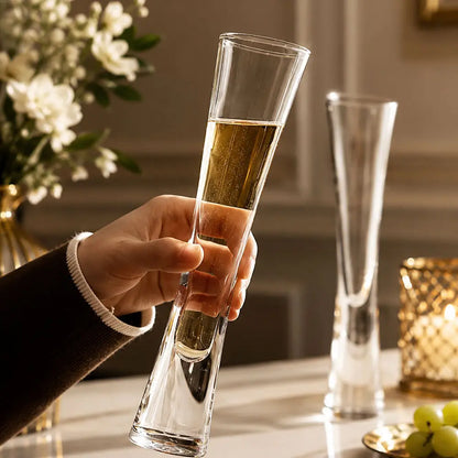 Hand holding one of two champagne glasses filled with a sparkling drink on a table with flowers, grapes and a candle.