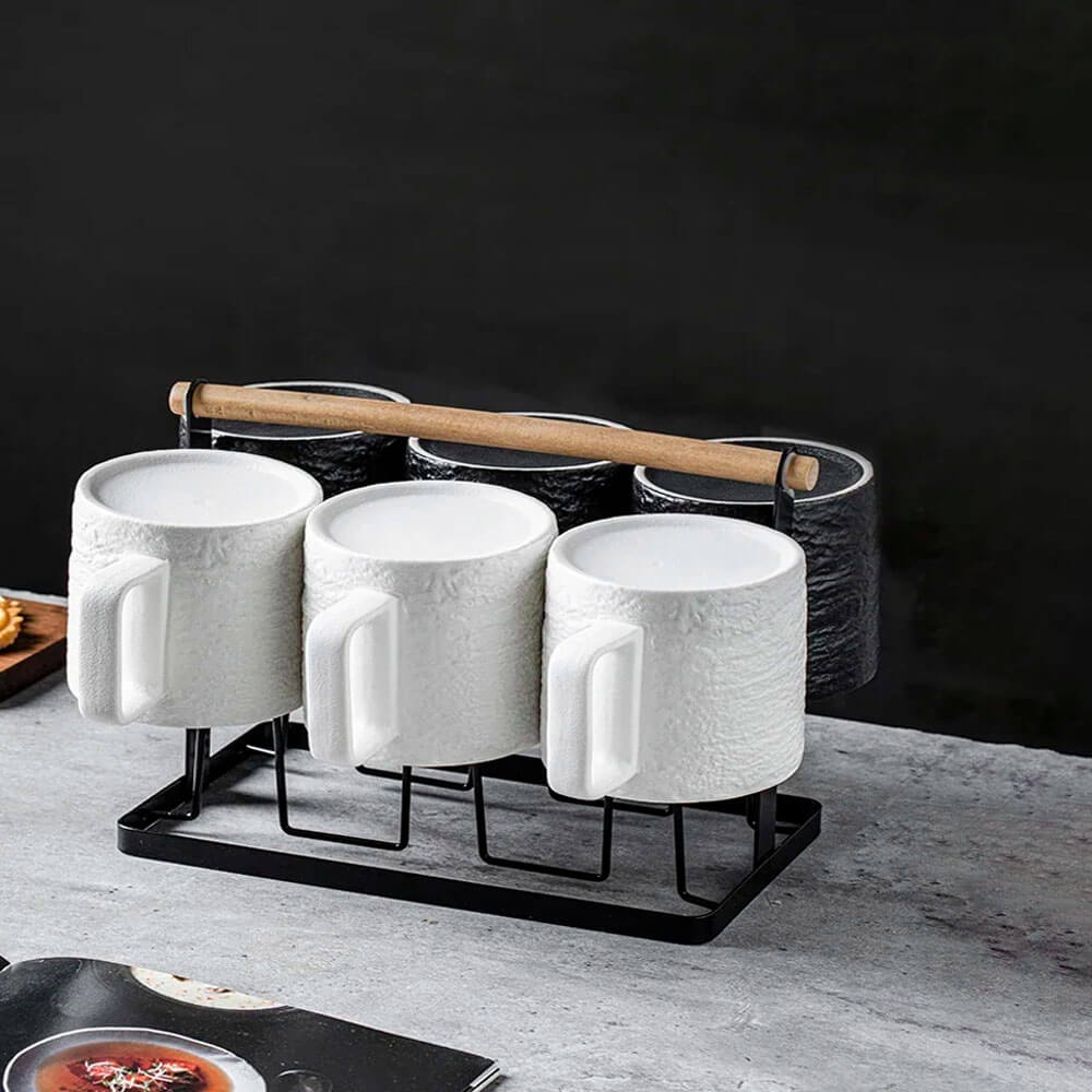 White and black coffee mug set with a black metal and wooden stand featuring six textured mugs neatly hanging from the holder.