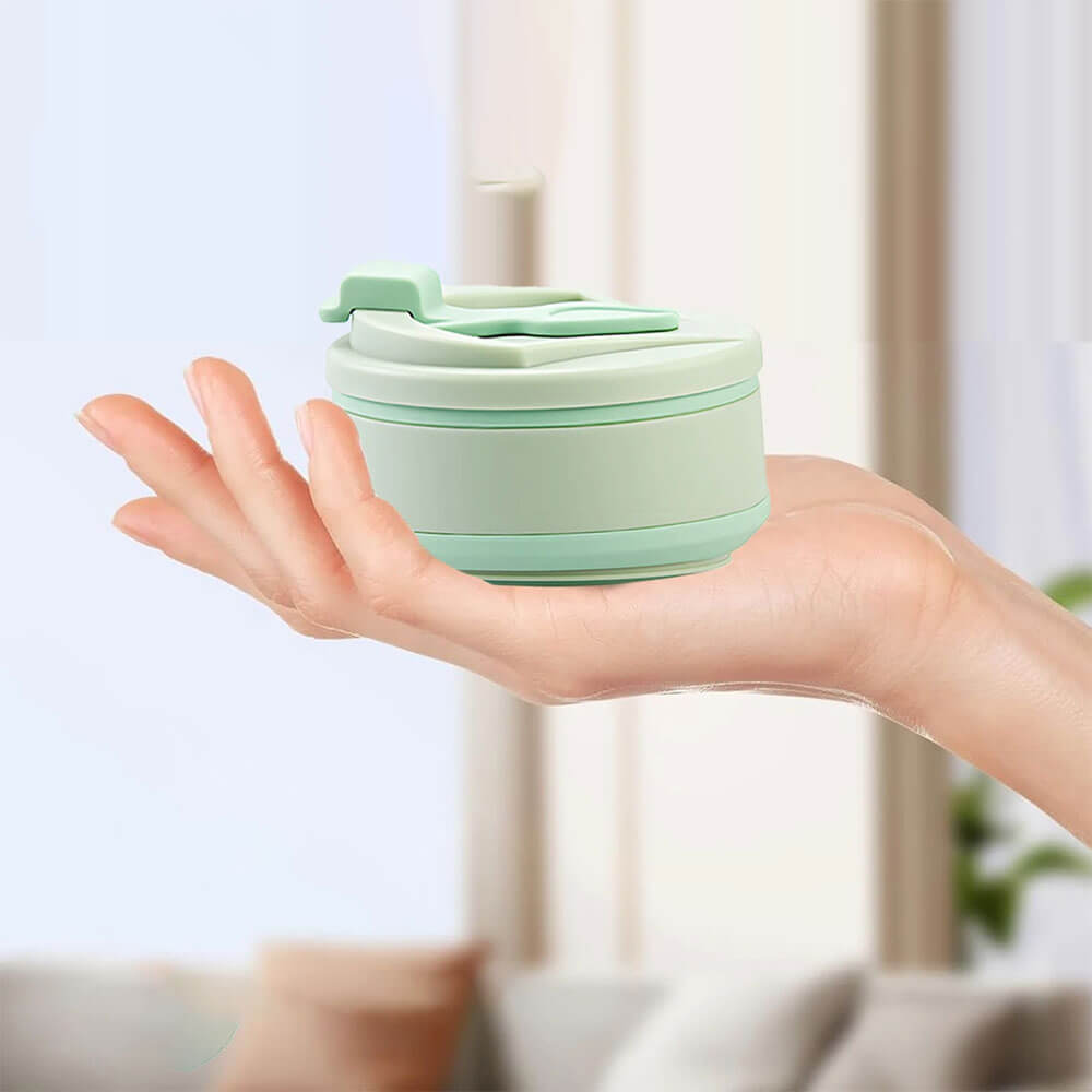 Mint green collapsible drink tumbler compactly folded and resting on an open hand, showcasing its lightweight and portable design perfect for easy storage and travel.