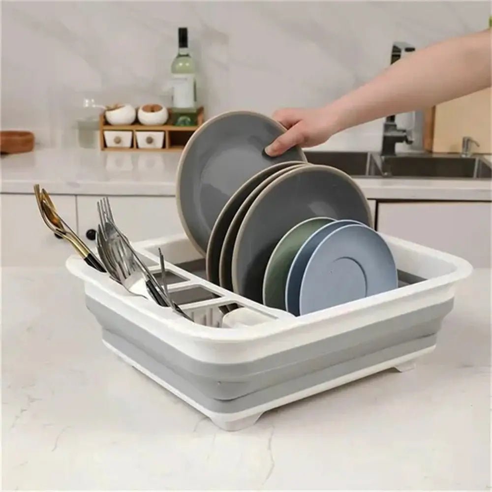 A person places gray plates into a white and gray collapsible drying rack dishes with utensils organized in side compartments on a kitchen counter.