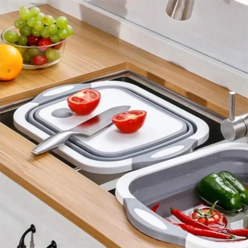 Collapsible sink cutting board with chopped tomato and knife on top, next to a basin rinsing peppers and tomatoes in the sink.