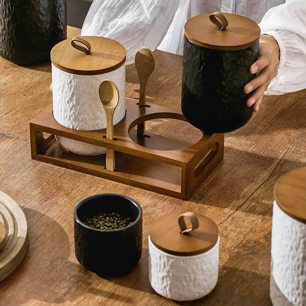 Elegant set of black and white ceramic condiment containers with lids, featuring natural wood accents and a wooden tray for organized kitchen storage.