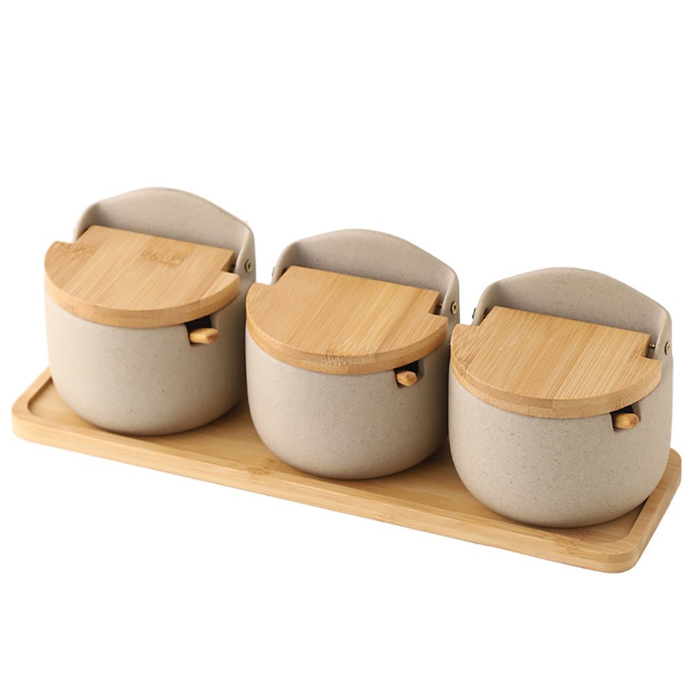 Set of three condiment jars with wooden lids on a wooden tray.