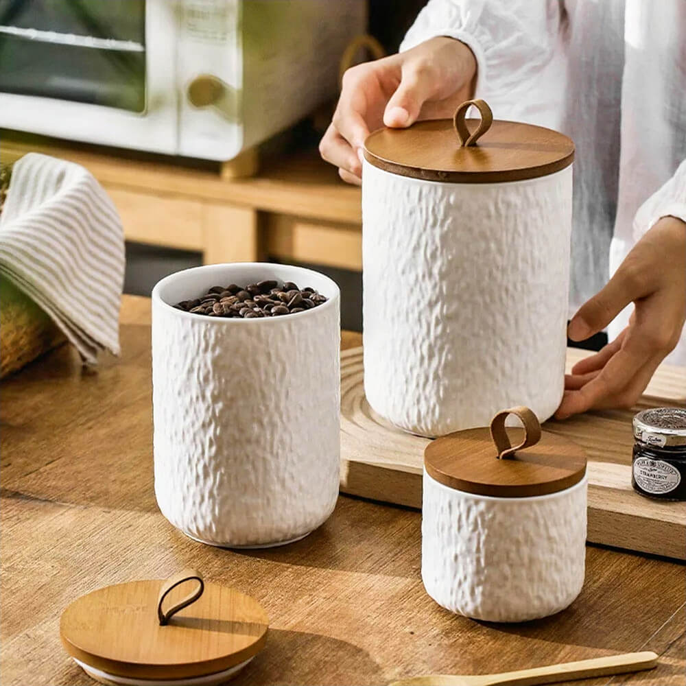 White ceramic condiment storage containers with textured finishes, natural wood lids, and a modern design, perfect for organizing kitchen essentials.