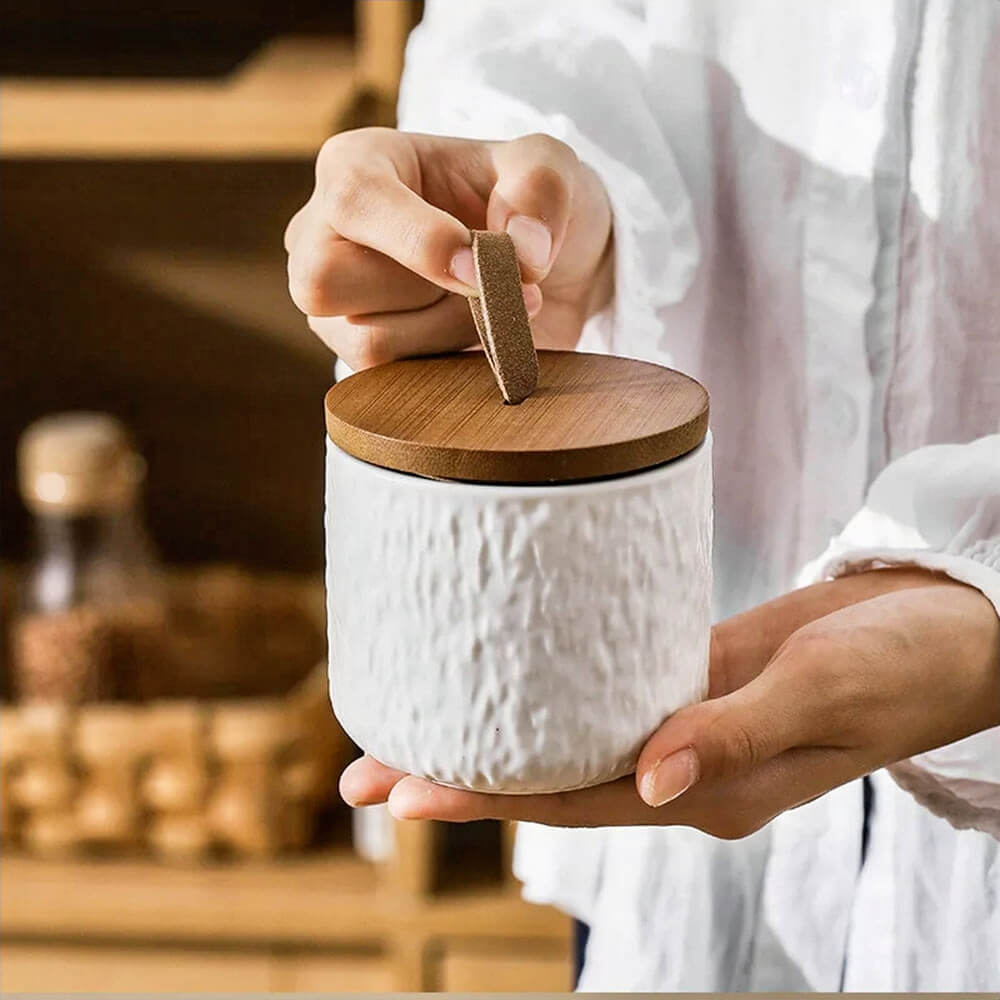 Close-up of a white ceramic condiments container set with a textured finish and natural wood lid, showcasing its elegant and functional design for kitchen storage.