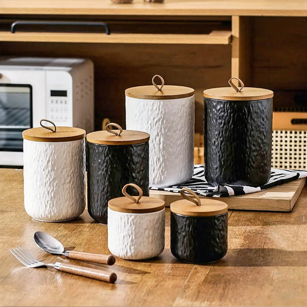 Set of black and white ceramic condiments containers with lids, featuring a textured finish and natural wood accents, perfect for stylish and functional kitchen organization.