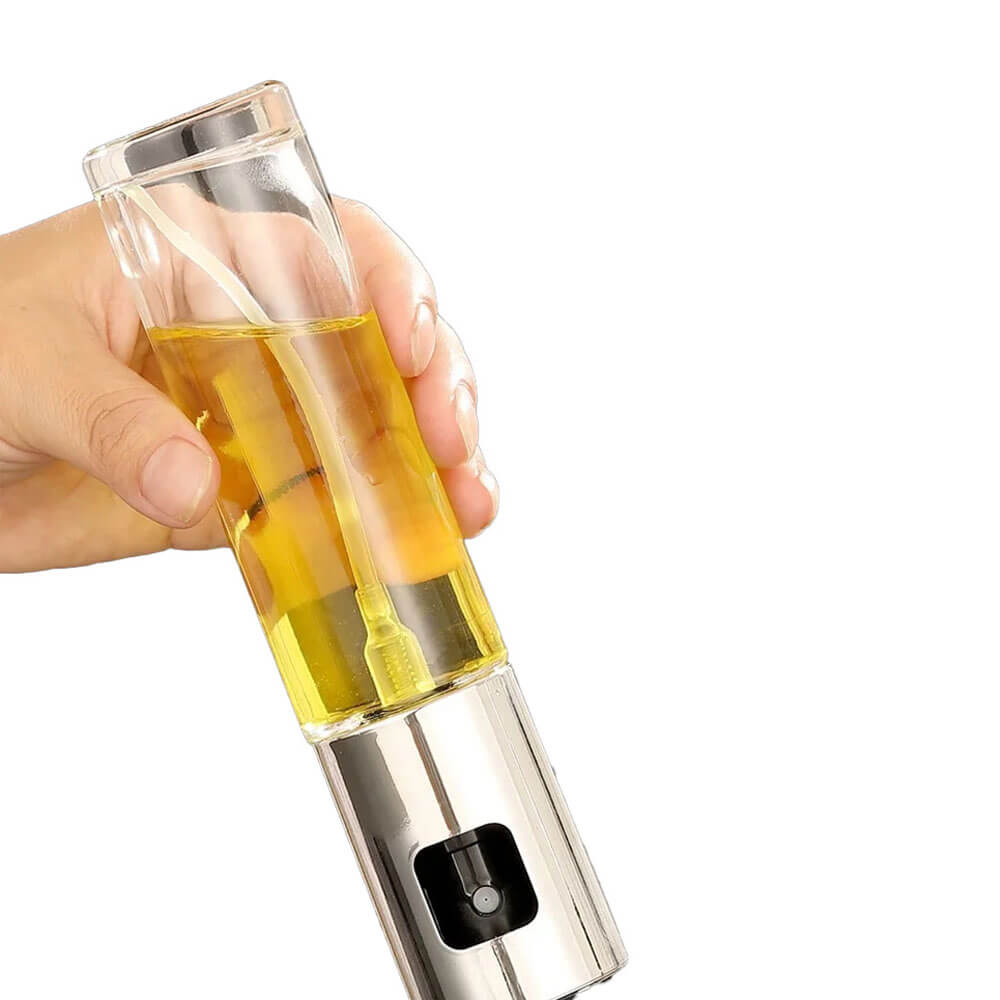 A hand holding a sleek glass cooking oil spray bottle with a stainless steel top. The bottle is filled with golden oil, showcasing its modern and functional design.