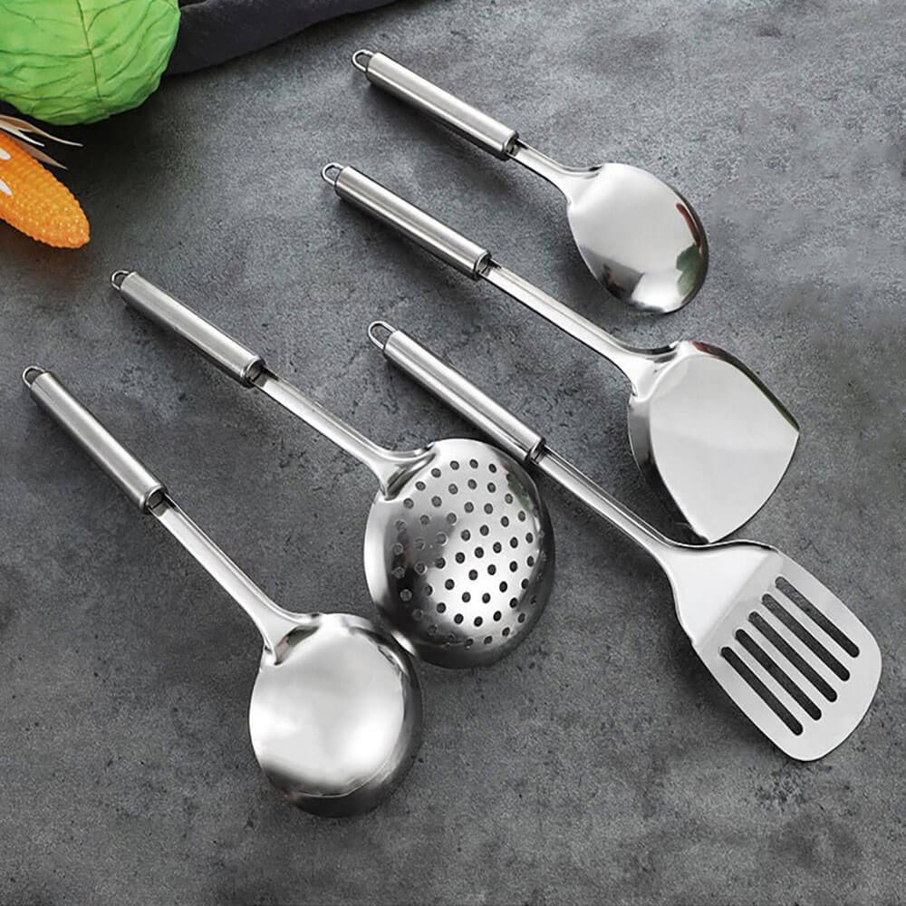 A set of five polished stainless steel cooking utensils arranged on a dark gray countertop. The set includes a ladle, slotted spoon, spatula, wok spatula, and serving spoon, each with a sleek and durable design. The ergonomic handles are smooth and feature hanging loops for convenient storage. In the background, fresh vegetables such as corn and cabbage add a vibrant and practical touch to the scene, emphasizing the utensils&