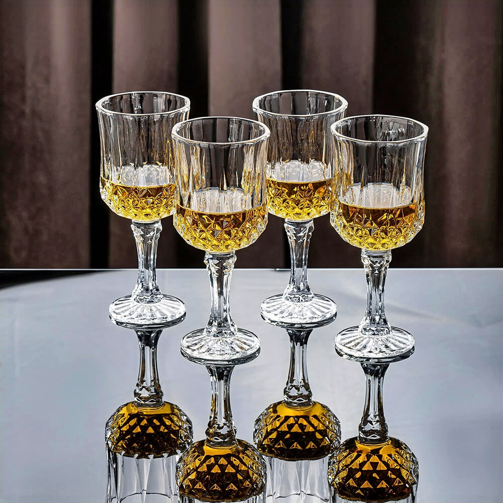 Four crystal cocktail glasses with a diamond-cut design, filled with amber liquid, displayed on a reflective surface.