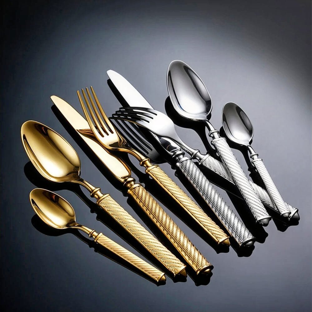 Cutlery flatware set in gold and silver with textured handles, includes forks, knives, and spoons arranged diagonally on black surface.