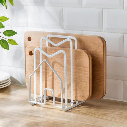 A stylish cutting board rack holder made of white metal, neatly organizing three wooden cutting boards of different sizes. The rack features a minimalistic, modern design with a house-shaped structure, resting on a wooden countertop with a white tiled backsplash in the background. Perfect for keeping cutting boards upright and accessible in the kitchen.