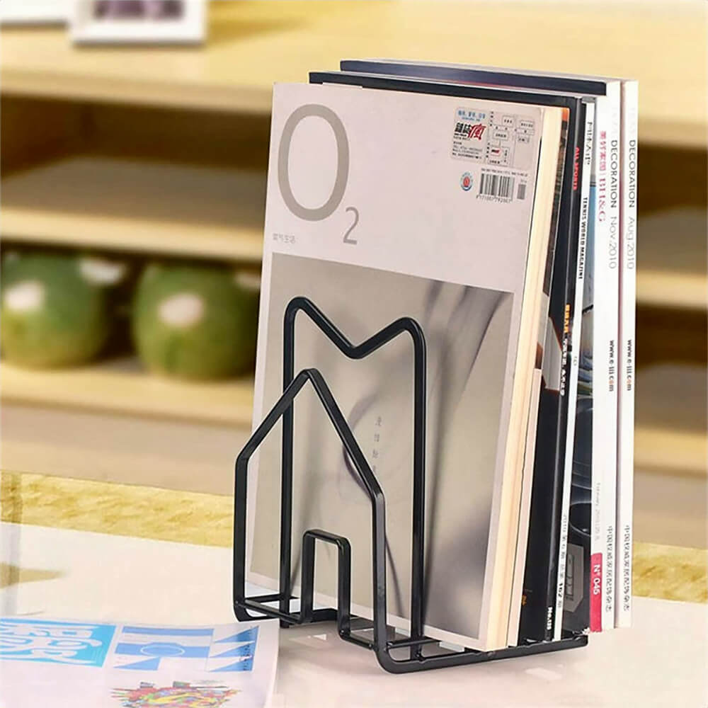 A multipurpose black cutting board storage rack with a sleek, house-shaped metal design. Although currently used to organize magazines upright, this rack is ideal for storing cutting boards neatly on kitchen countertops. Its sturdy and compact structure makes it a versatile organizer for various items in the home.