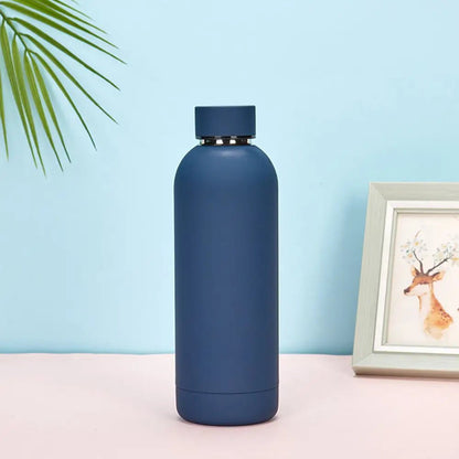 Blue water bottle on a light pink surface with a light blue background and a framed picture of a deer.