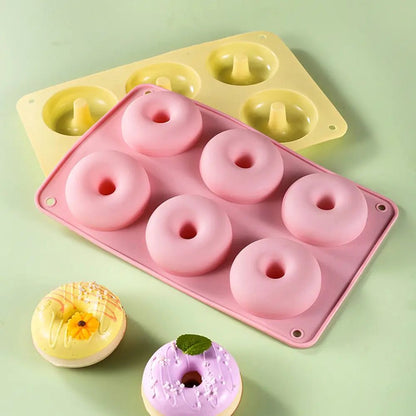 Two silicone doughnut pans in pink and yellow, each with six round molds, shown alongside decorated baked doughnuts.